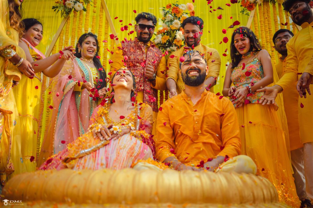 Candid Photography of Bride & groom with thier friends and family behind them showering them with flowers on haldi ceremony